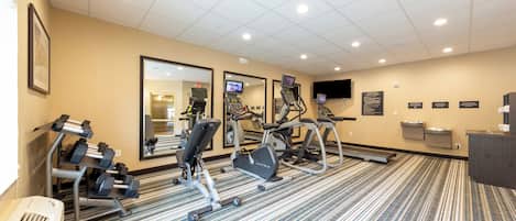 A hotel fitness center with cardio machines, dumbbells, and a mirrored wall.