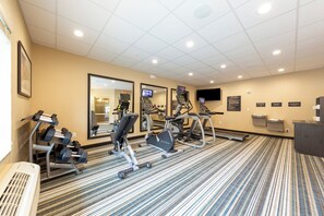 Un gimnasio hotelero con máquinas de cardio, mancuernas y un espejo grande.