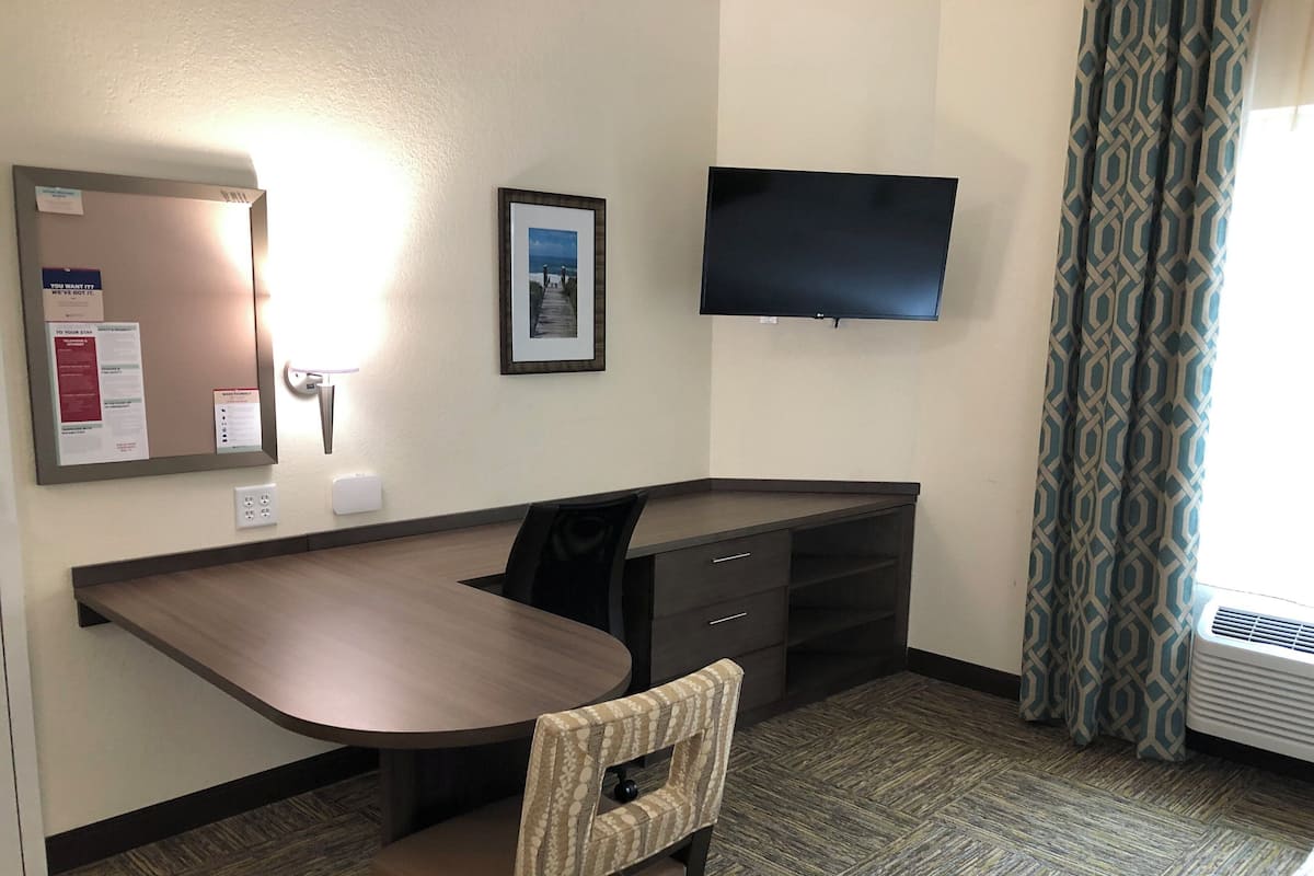 Une chambre d’hôtel équipée d’un bureau, d’une chaise, d’un téléviseur à écran plat et d’un tableau encadré au mur.