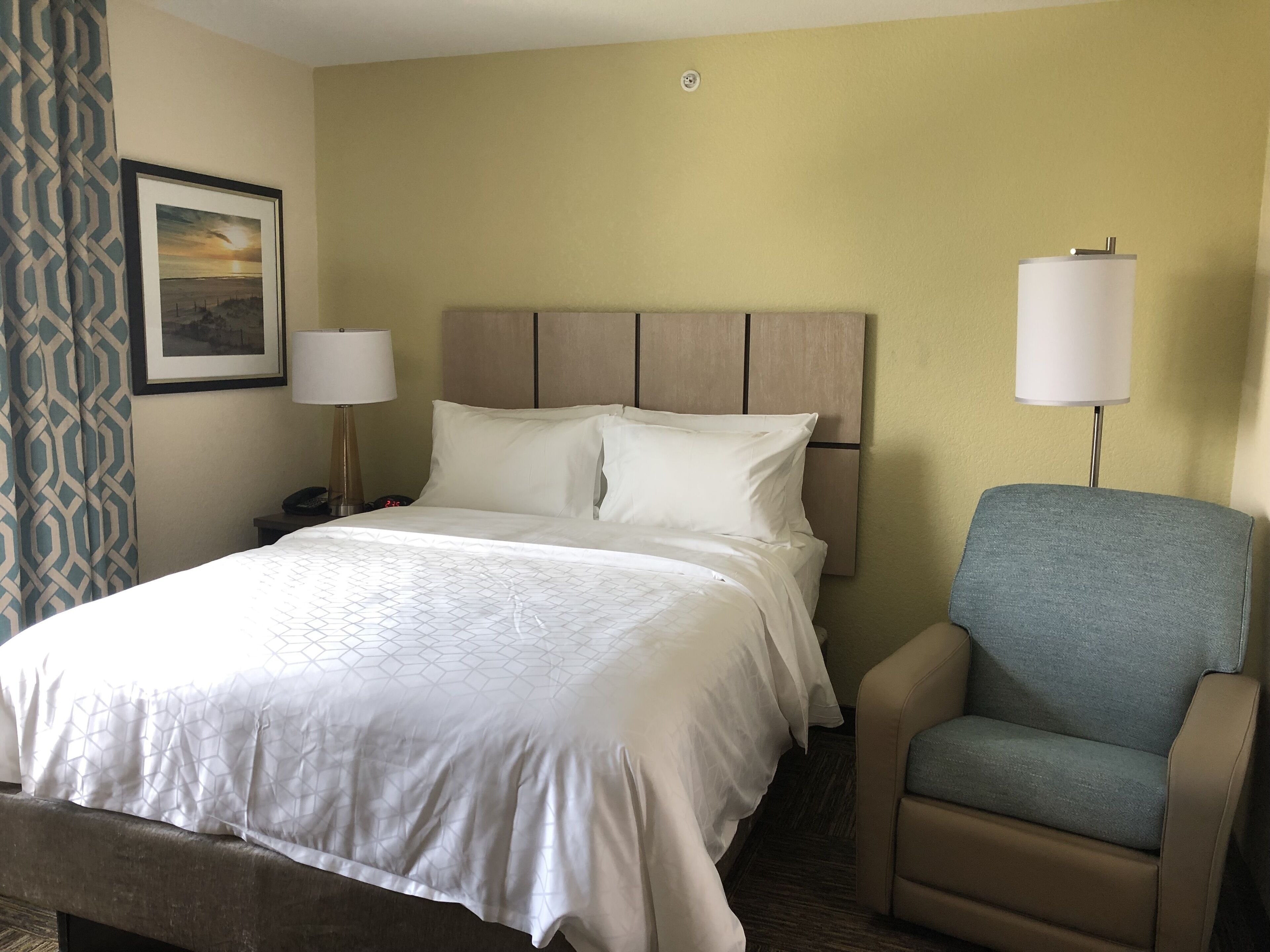 Een hotelkamer met een bed, twee bedlampen, een stoel en een wandklok.