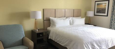 Ein Hotelzimmer mit einem Bett, zwei Nachttischen mit Lampen, einem Sessel und einem gerahmten Bild an der Wand.