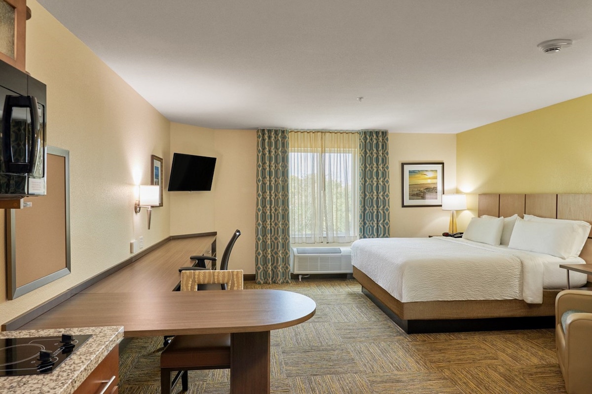 A hotel room with a bed, bedside table, TV, and a desk with a chair.