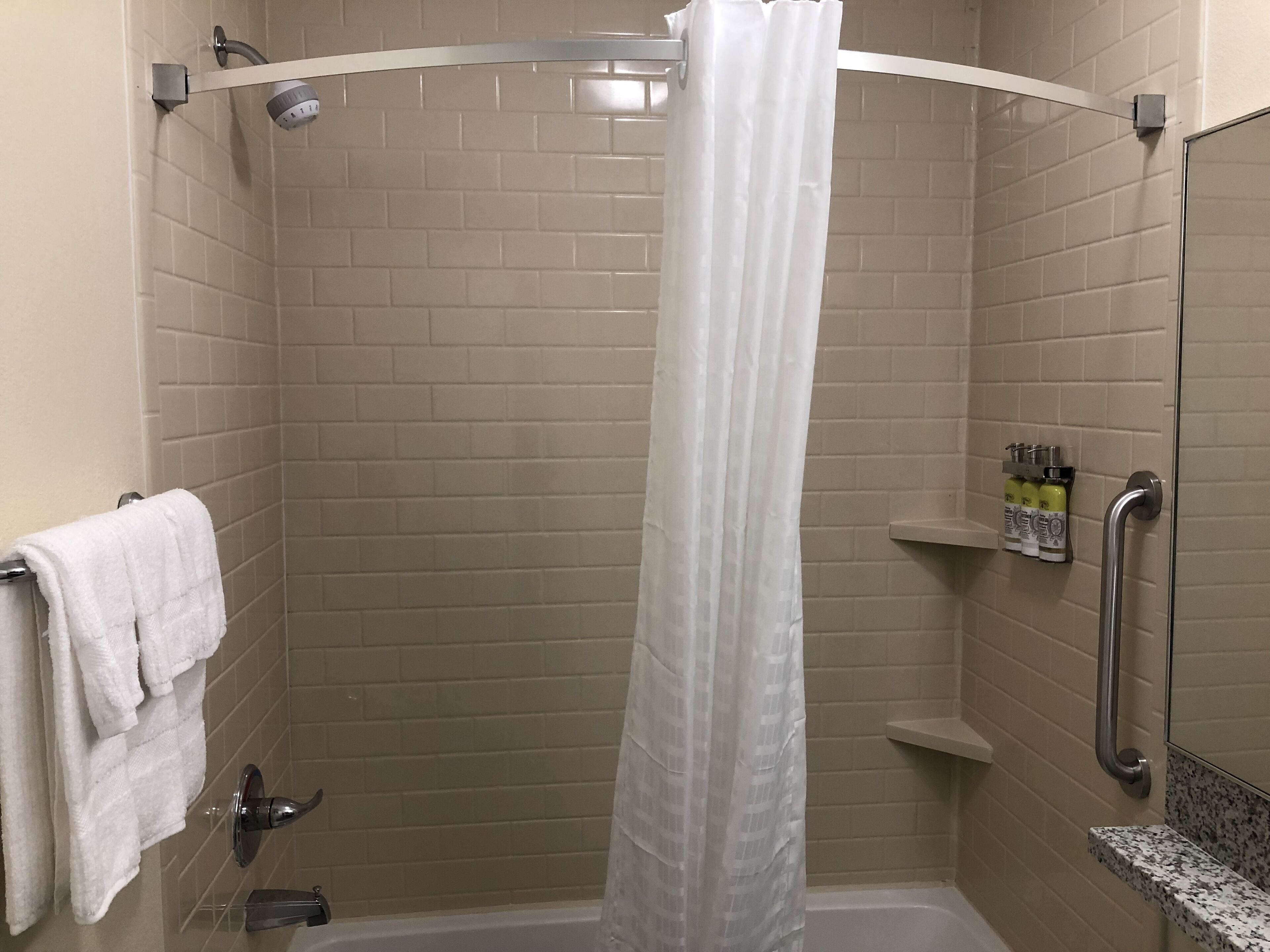A shower with a white curtain, a handrail, and a shelf with toiletries.