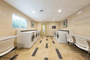 A laundry room with multiple washing machines, a drying rack, and a mirror. - Candlewood Suites Panama City Beach Pier by IHG (Panama City Beach)