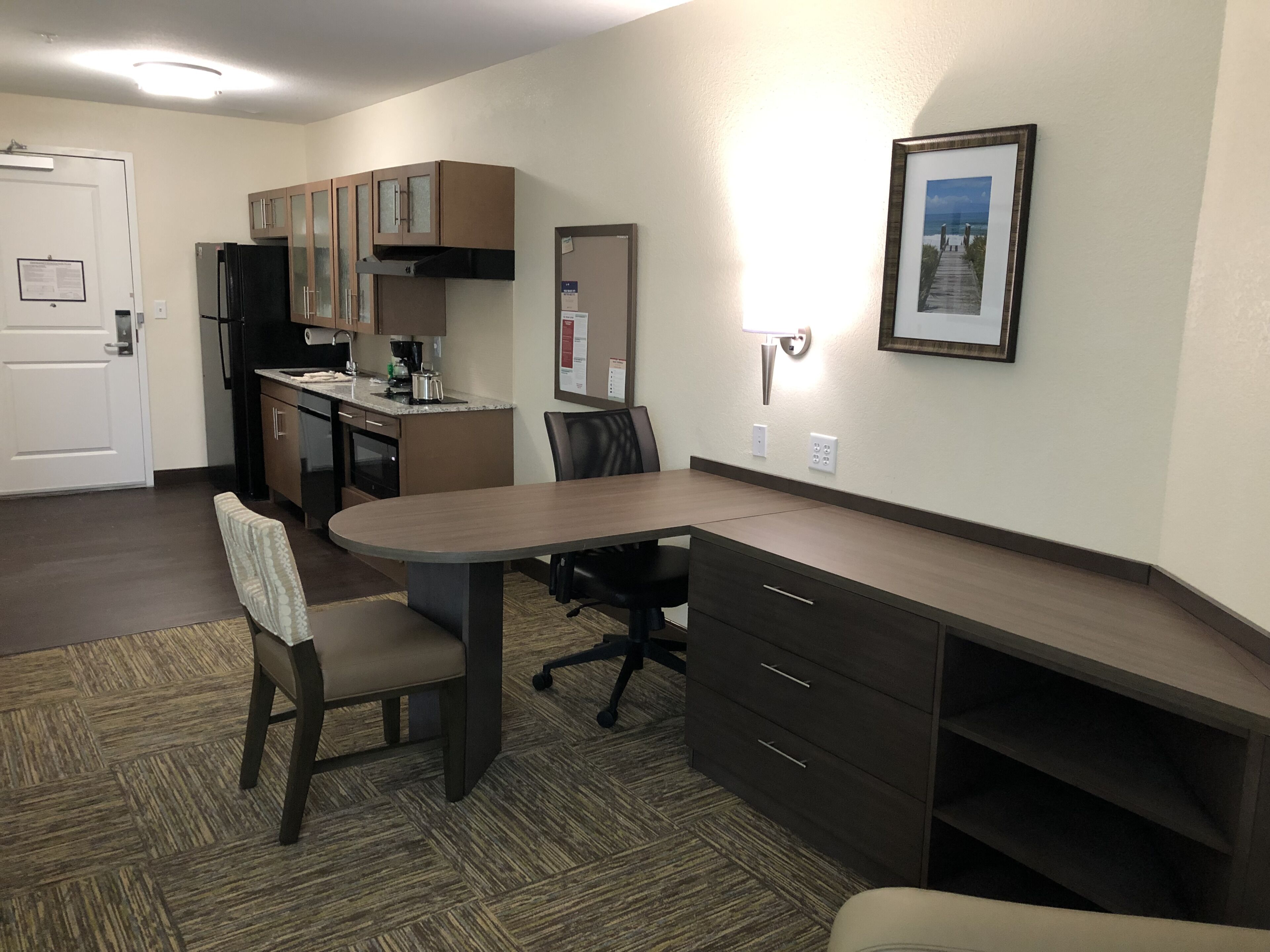 A compact kitchen with modern appliances, a dining area with a table and chairs, and a framed picture on the wall.