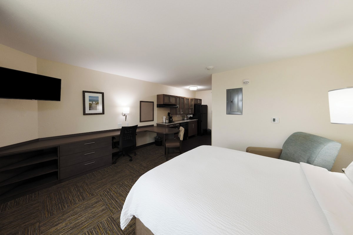 Une chambre d’hôtel dotée d’un grand lit, d’un bureau avec une chaise, d’une kitchenette et d’un téléviseur à écran plat fixé au mur.
