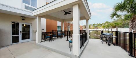 Un espace extérieur aménagé en terrasse, avec des tables et des chaises, un ventilateur de plafond et un chariot-barbecue.