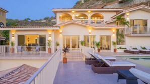 Ein zweigeschossiges Haus mit Swimmingpool, Sitzgelegenheiten im Freien und einem Balkon.