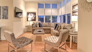 Un salon moderne comprenant un canapé d’angle, deux fauteuils, une table basse et un téléviseur fixé au mur.