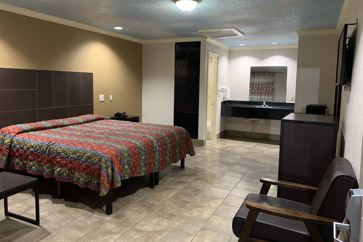 A hotel room with a bed, a desk, a chair, a bathroom with a sink, and a mirror.