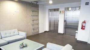 A modern waiting area with a sofa, a glass-top table, and a white wall with a fire extinguisher. - Pet Friendly Apart(9 Person max)+Pool+Grill+Billiards+Gym (Lince)