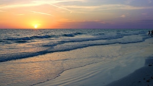 Une plage avec des vagues au coucher du soleil, un ciel dégagé et quelques personnes au loin.