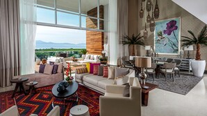 A spacious living room with a large window, a sofa set, a coffee table, and a dining area with chairs and a table.