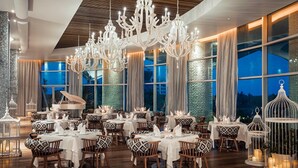 A spacious dining area with multiple tables, elegant chandeliers, and large windows offering a view of the cityscape.