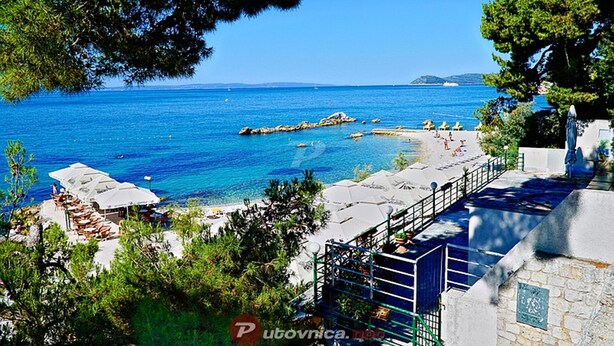Vista sulla costa con spiaggia, ombrelloni e un edificio in pietra.