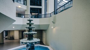 Une fontaine à plusieurs niveaux, située dans un vaste espace intérieur doté d’un haut plafond et d’un balcon donnant sur cet espace.