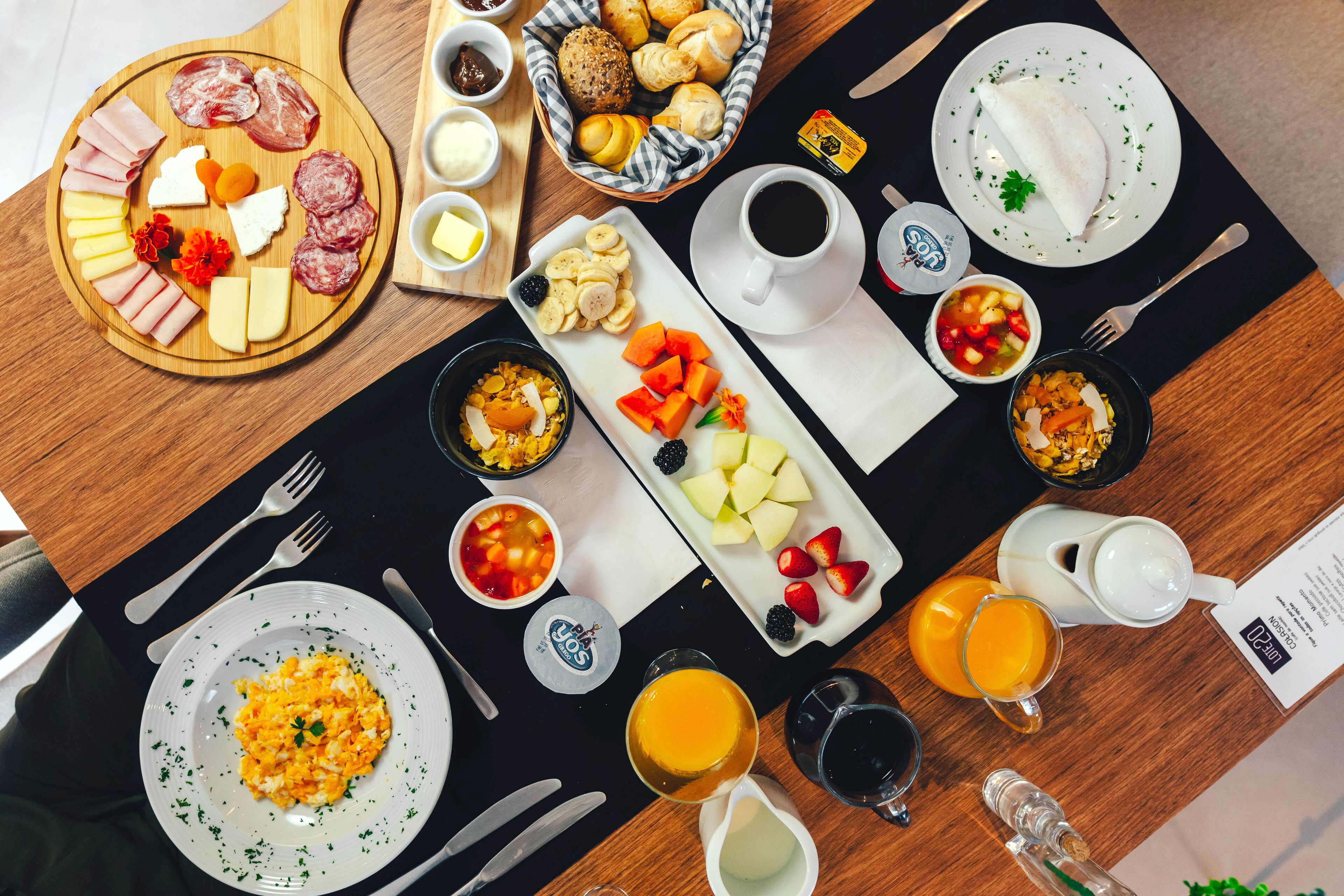 Desayuno con diversas comidas, bebidas y utensilios sobre una mesa.