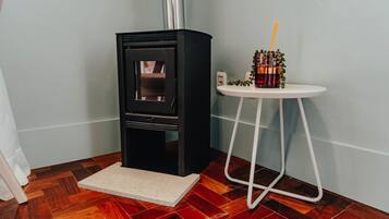 Una habitación de esquina con chimenea de leña, una pequeña mesa blanca con una bebida y suelo de madera.