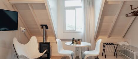 A cozy attic room with a white ceiling, a fireplace, a TV, and a small table with chairs.