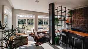Eine moderne Bar mit Holztresen und Hockern, einem großen Fenster mit Ausblick ins Freie und einem Regal mit Flaschen.