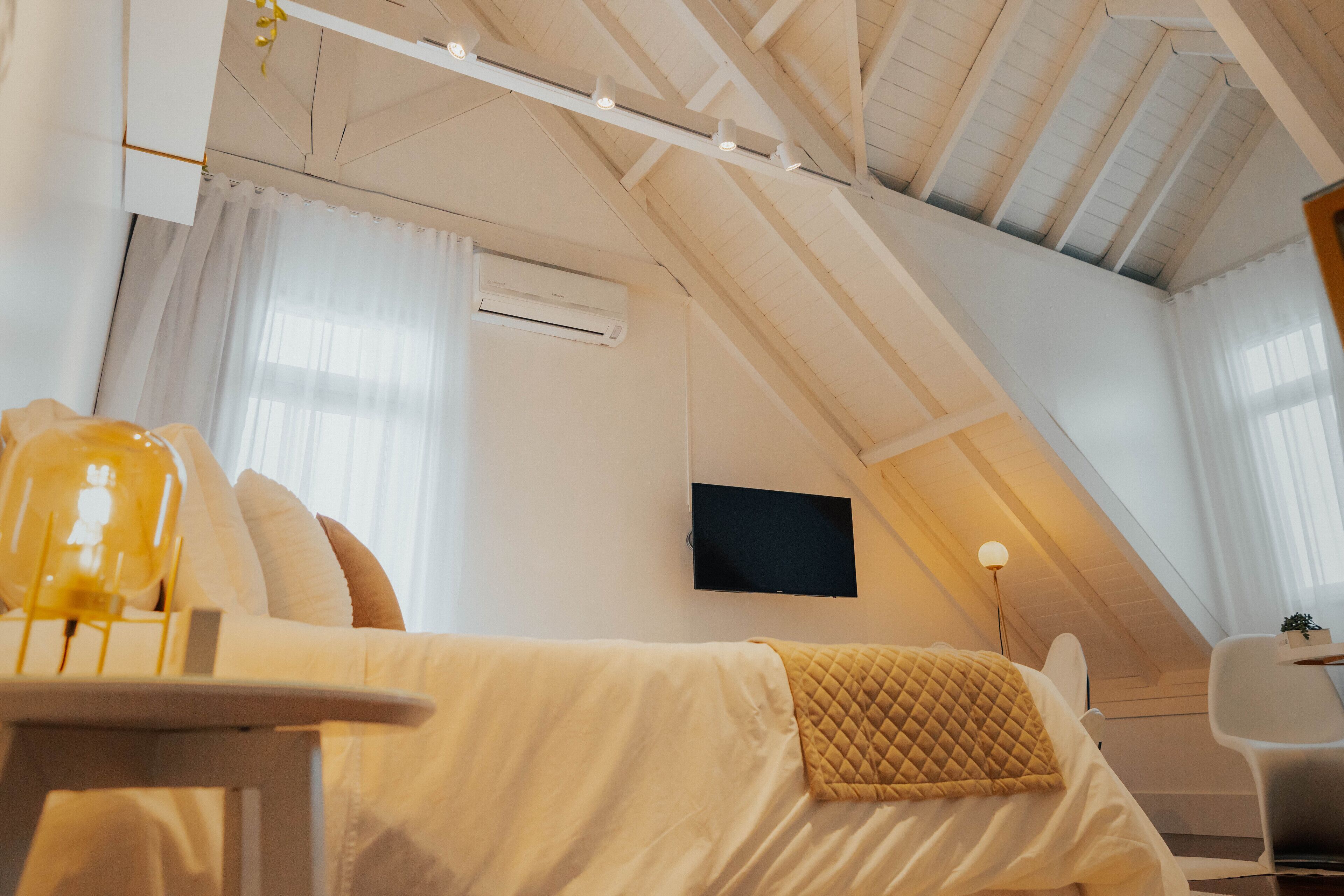 A cozy, well-lit attic bedroom with a bed, a desk, and a chair.