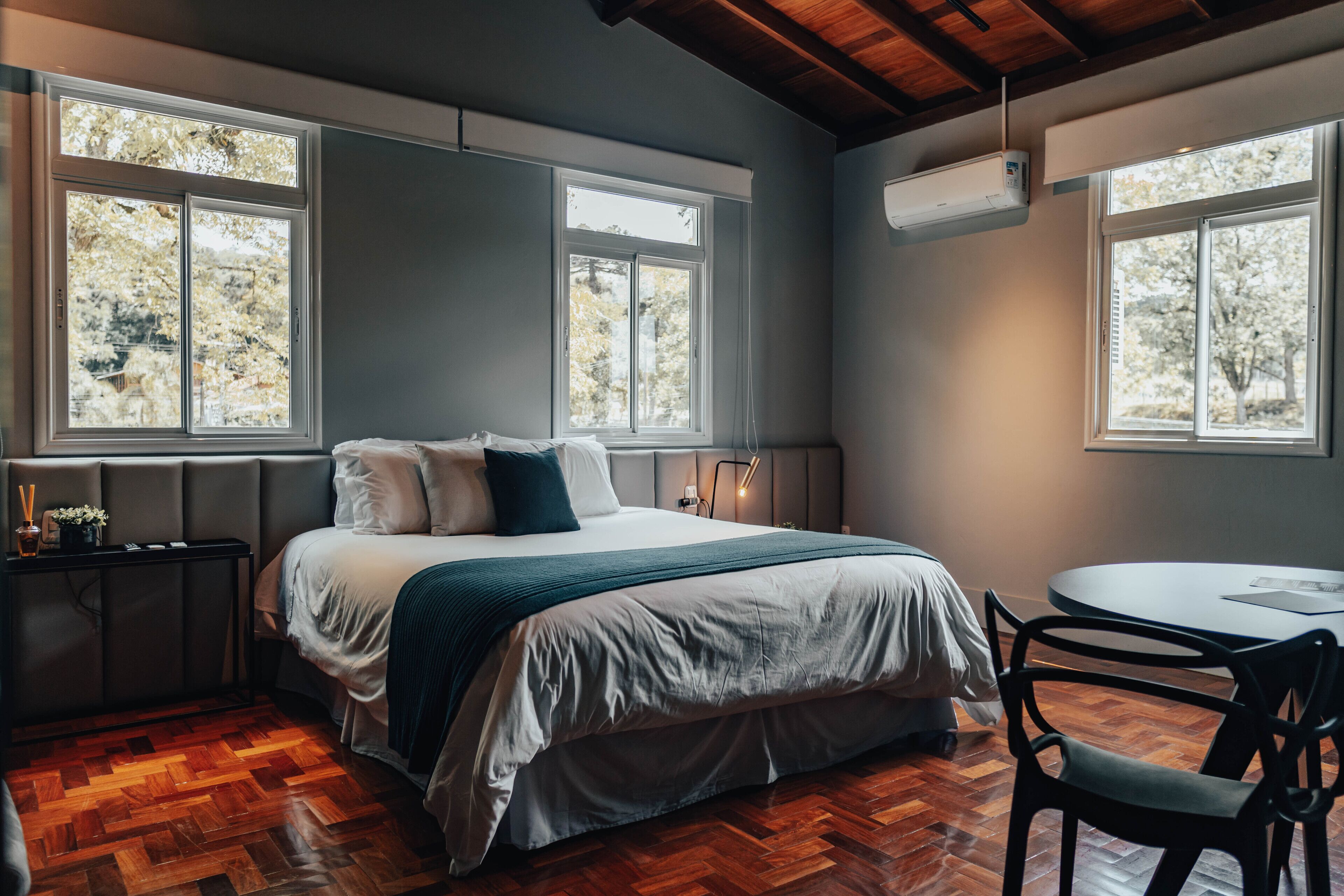 Un dormitorio con cama, mesita de noche, silla y ventana con vista a árboles.