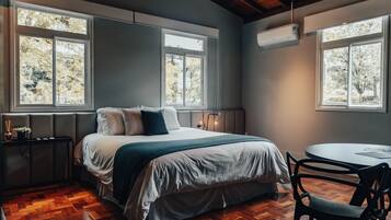 Un dormitorio con cama, mesita de noche, silla y ventana con vista a árboles.