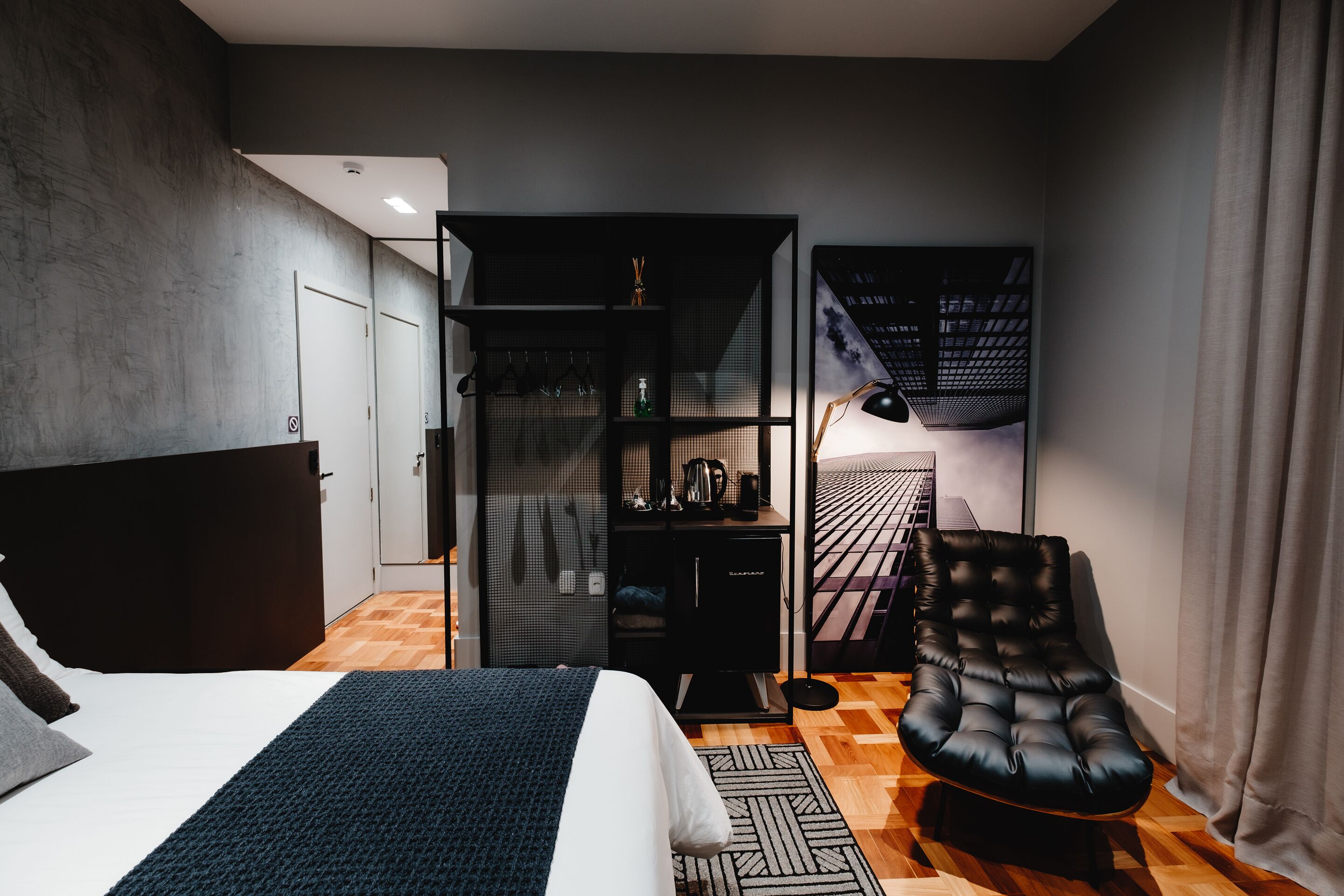 Quarto moderno com cama, uma poltrona de couro preto, guarda-roupa e escrivaninha com luminária.