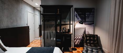 Quarto moderno com cama, uma poltrona de couro preto, guarda-roupa e escrivaninha com luminária.