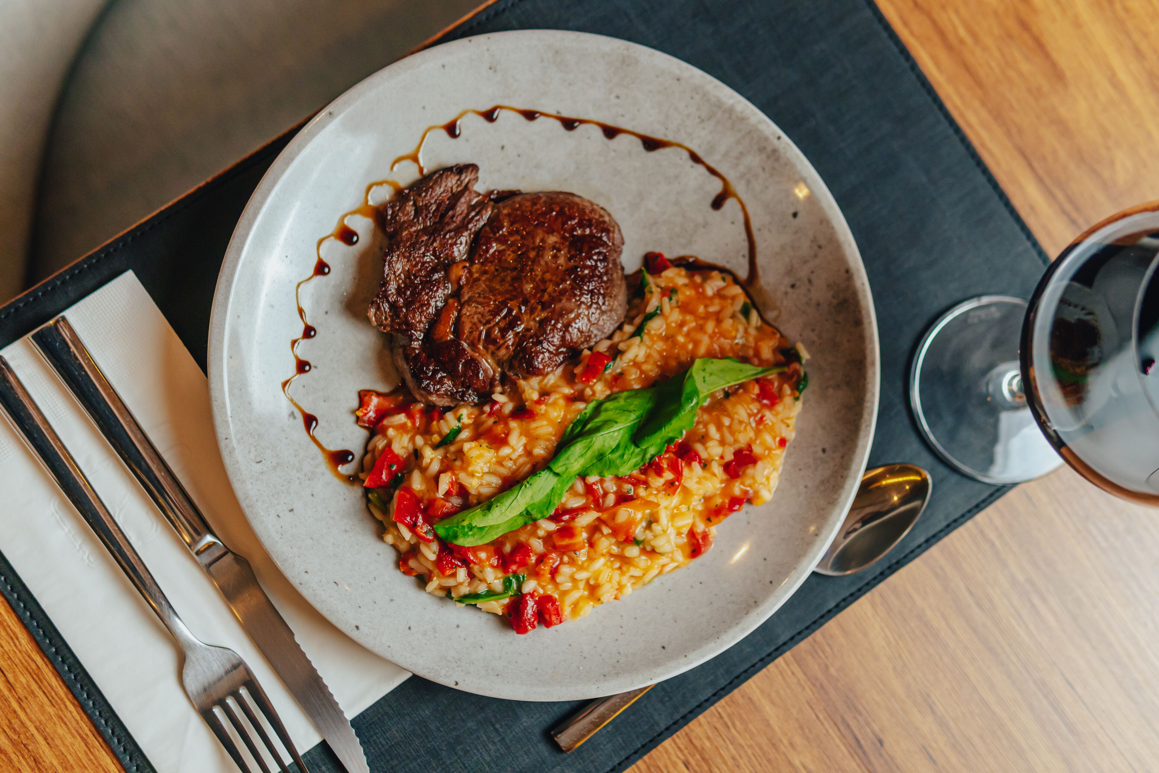 Prato com bife e risoto, acompanhado por um copo de vinho tinto.