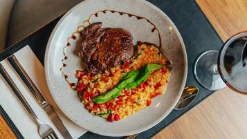 Prato com bife e risoto, acompanhado por um copo de vinho tinto.