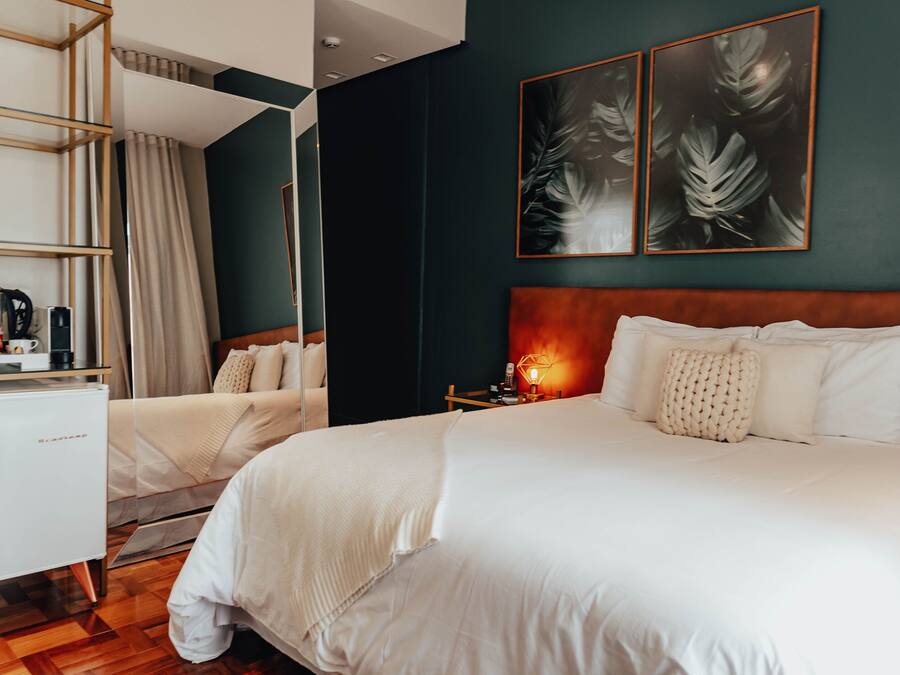 Habitación de hotel con una cama grande, una mesita de noche con lámpara, un armario y un escritorio con cafetera.