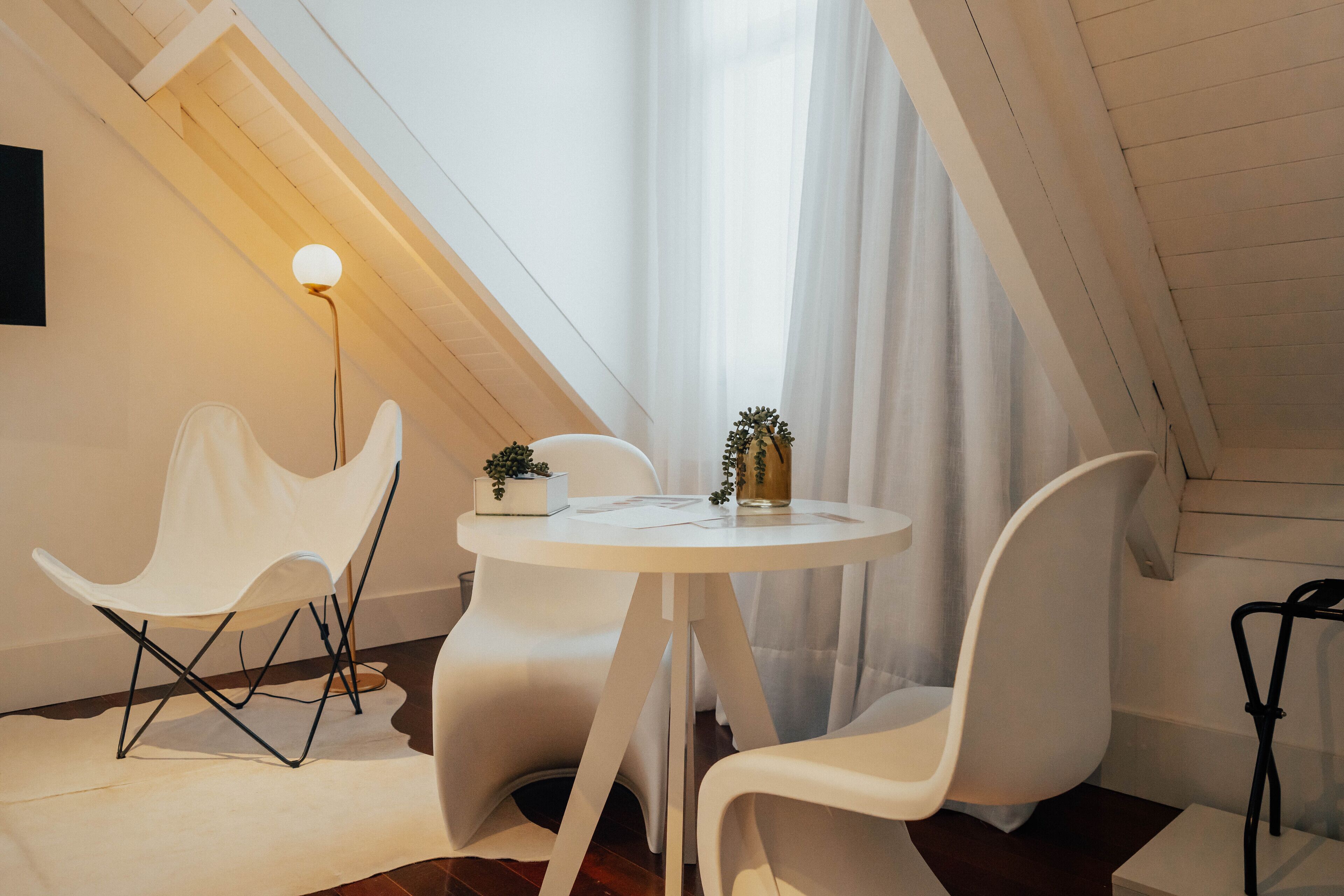 Una habitación moderna y bien iluminada, con una mesa redonda, sillas blancas y una planta pequeña sobre la mesa.