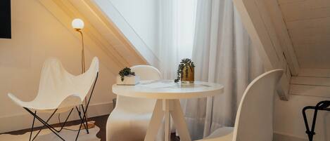 Una habitación moderna y bien iluminada, con una mesa redonda, sillas blancas y una planta pequeña sobre la mesa.