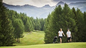En golfbane med et bjergrigt baggrundsmotiv, frodig vegetation og en klar himmel.