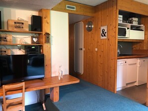 A compact kitchen with wooden cabinets, a microwave, a refrigerator, and a small dining area with a table and chair.