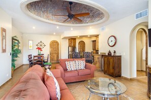 Un salon spacieux doté d’un ventilateur de plafond, d’une table basse en verre et d’un coin salon confortable.