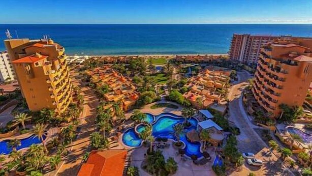 Un resort con varias construcciones, un área de piscina central y vistas al océano.
