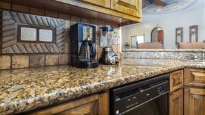 Una cocina con encimeras de granito, armarios de madera, cafetera, licuadora y lavavajillas.