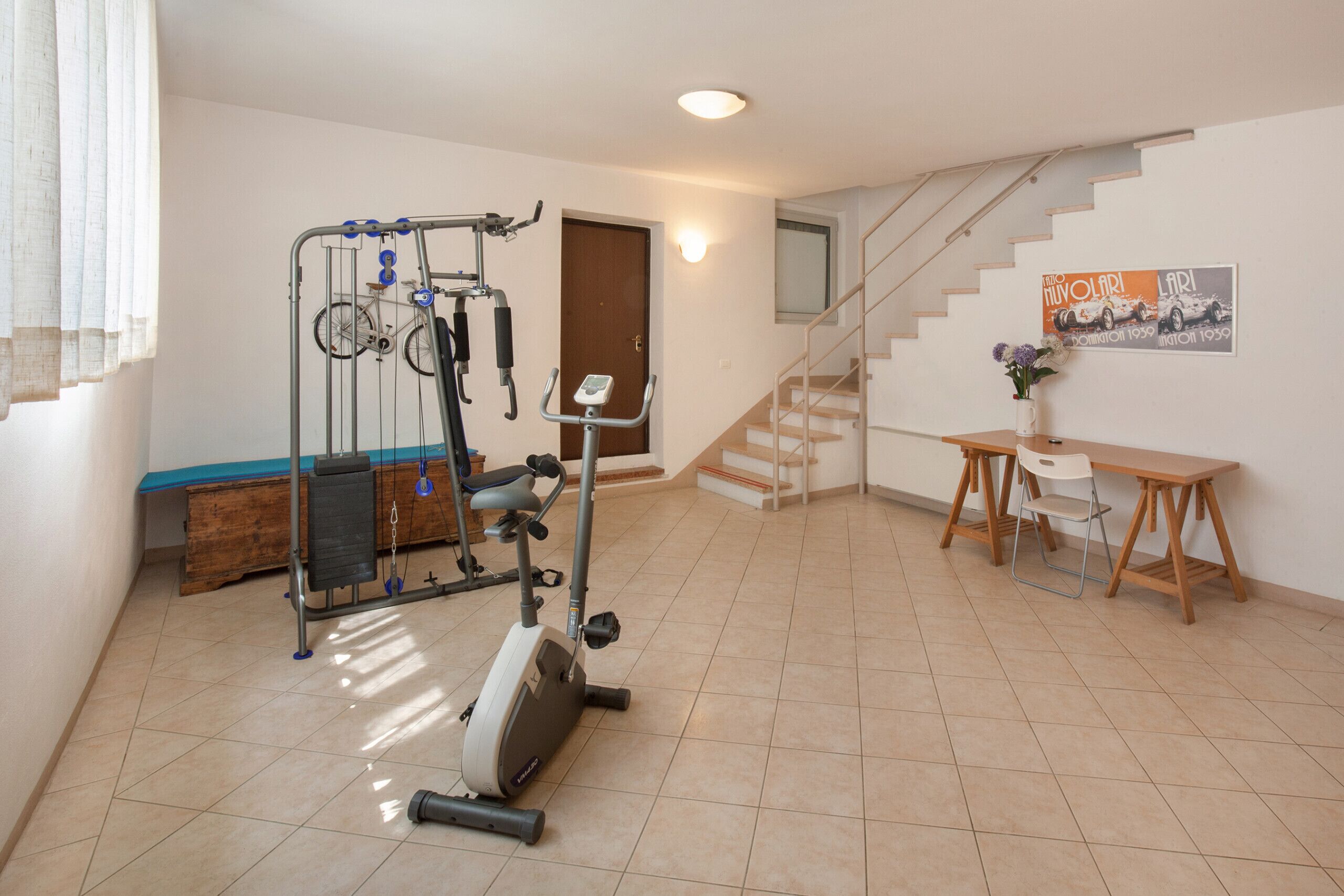 Une salle de sport à domicile équipée de matériel d’exercice, d’un banc en bois et d’un escalier menant à l’étage supérieur.