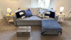 A grey sofa with striped cushions, a matching ottoman, and two nightstands with lamps.
