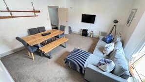A living room with a wooden dining table, grey sofa, and a striped ottoman.