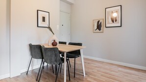 Ein Essbereich mit einem Holztisch und vier Stühlen, einer Vase mit getrockneten Blumen sowie zwei gerahmten Kunstwerken an der Wand.