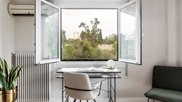 Ein Zimmer mit großem Fenster, Heizkörper, Schreibtisch, Stuhl und einer Topfpflanze.