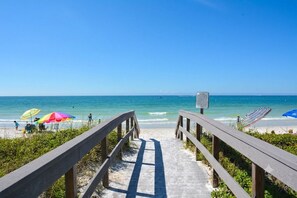 A wooden boardwalk leading to a beach with umbrellas and a sign.