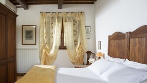 A bedroom with a bed, wooden headboard, a nightstand, a lamp, and a window with curtains. - B&B with Pool and view of Assisi (Bastia Umbra/Assisi)