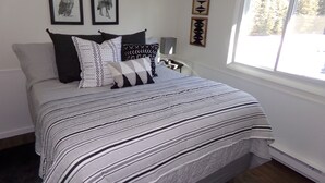 Une chambre à coucher avec un lit, des oreillers, une fenêtre et des œuvres d’art mural.