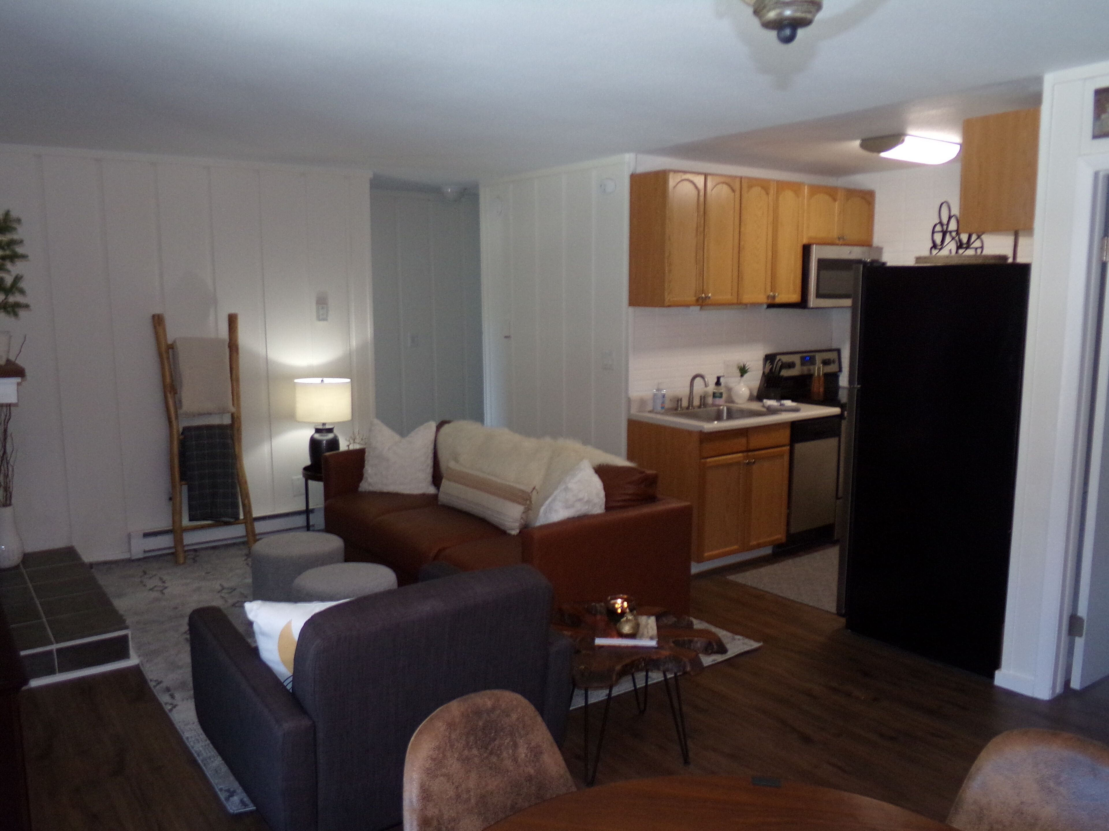 A compact living space with a kitchenette, a sofa, a dining table, and a ladder against the wall.