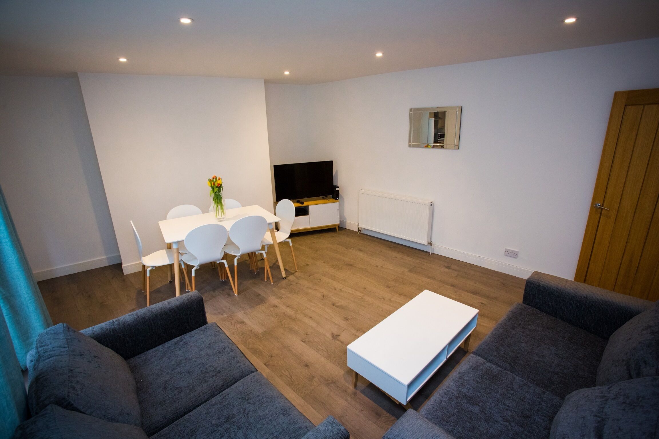 A modern living room with a dining area, grey sofas, a white coffee table, and a TV.