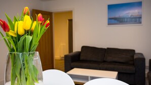 Un salón con un jarrón de tulipanes sobre una mesa blanca, un sofá marrón oscuro y un cuadro en la pared.